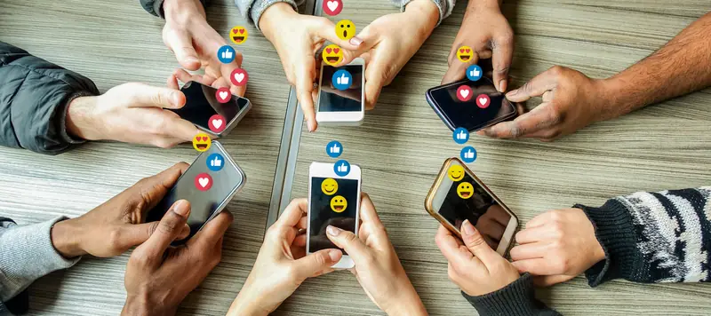 Pessoas usando celulares com ícones de curtidas e reações das redes sociais